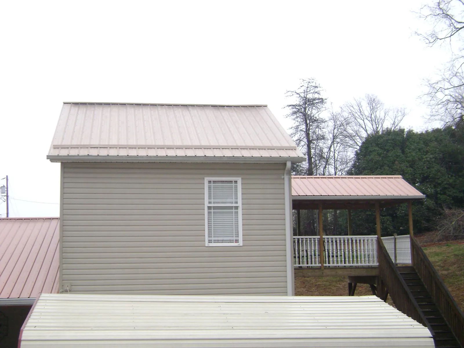 Tan metal roofs on a two story addition and attached porch, from a Roof Replacement job in Mount Pleasant